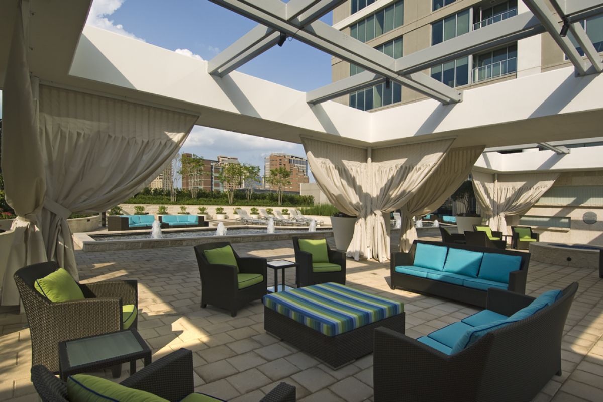 Modern outdoor lounge with blue and green seating, cabanas, and a fountain under a pergola.