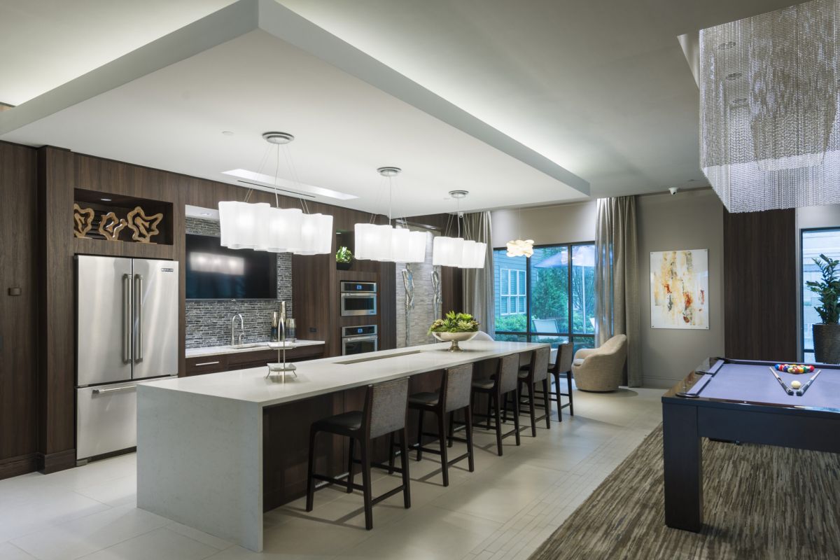 Modern kitchen with a long island, pendant lights, stainless appliances, and a pool table nearby.