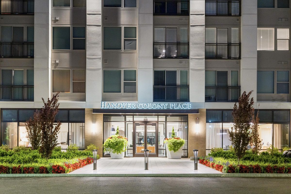 Entrance of a modern apartment building at night, with "Hanover Colony Place" signage and well-lit surroundings.