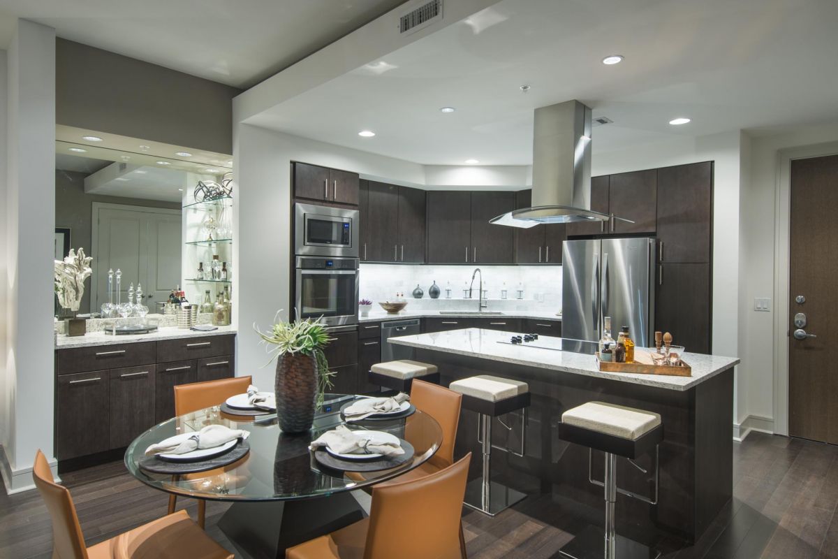 Hanover Company Modern kitchen with dark wood cabinets, island with stools, and round table set for three. Track lighting overhead.