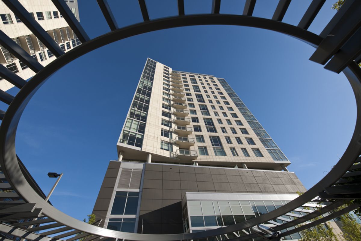High-rise building viewed through a circular metal frame against a clear blue sky.