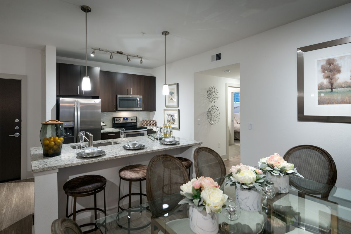 Modern kitchen and dining area with glass table, flower centerpieces, and stainless steel appliances.