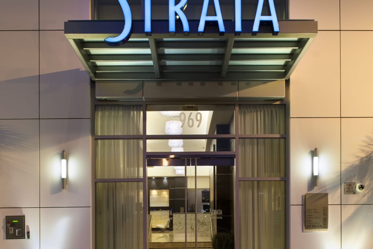 Building entrance with glass doors and a blue "STRATA" sign above, lit at night.