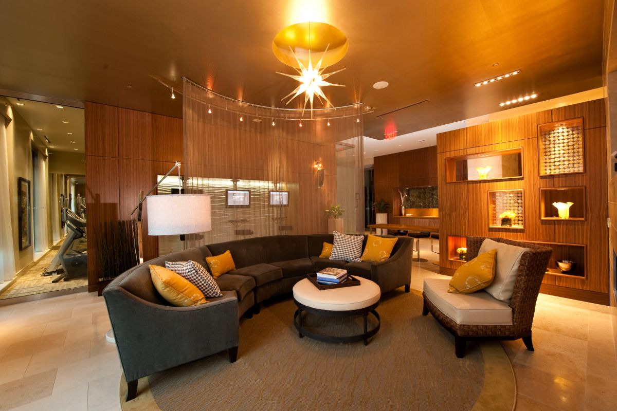 Modern lounge with curved sofa, round coffee table, accent chairs, warm lighting, and wood-paneled walls.