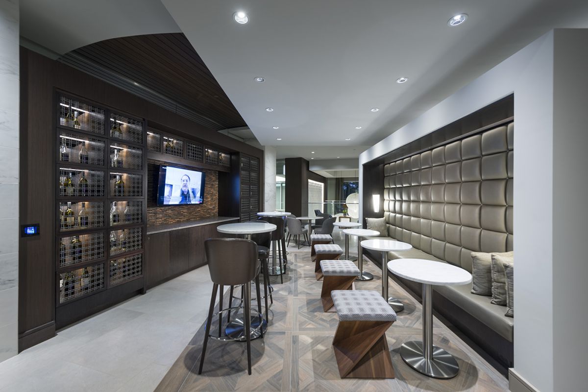 Modern lounge with round tables, cushioned bench seating, bar stools, and a wall-mounted TV.