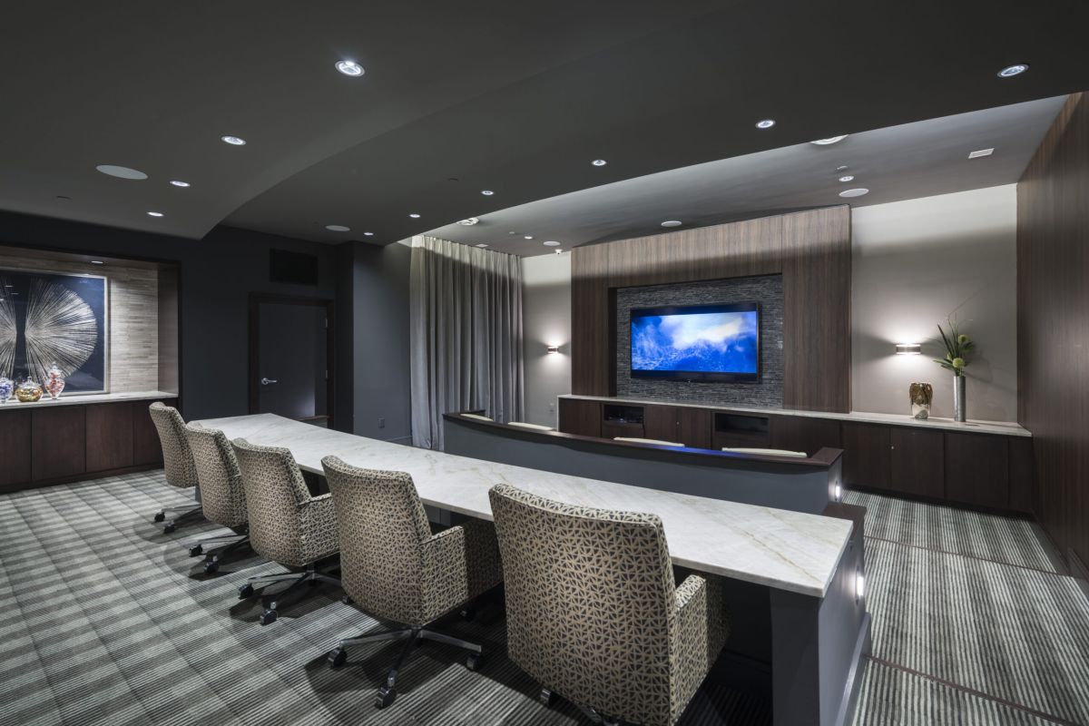 Modern conference room with a long marble table, patterned chairs, and a large wall-mounted TV screen.