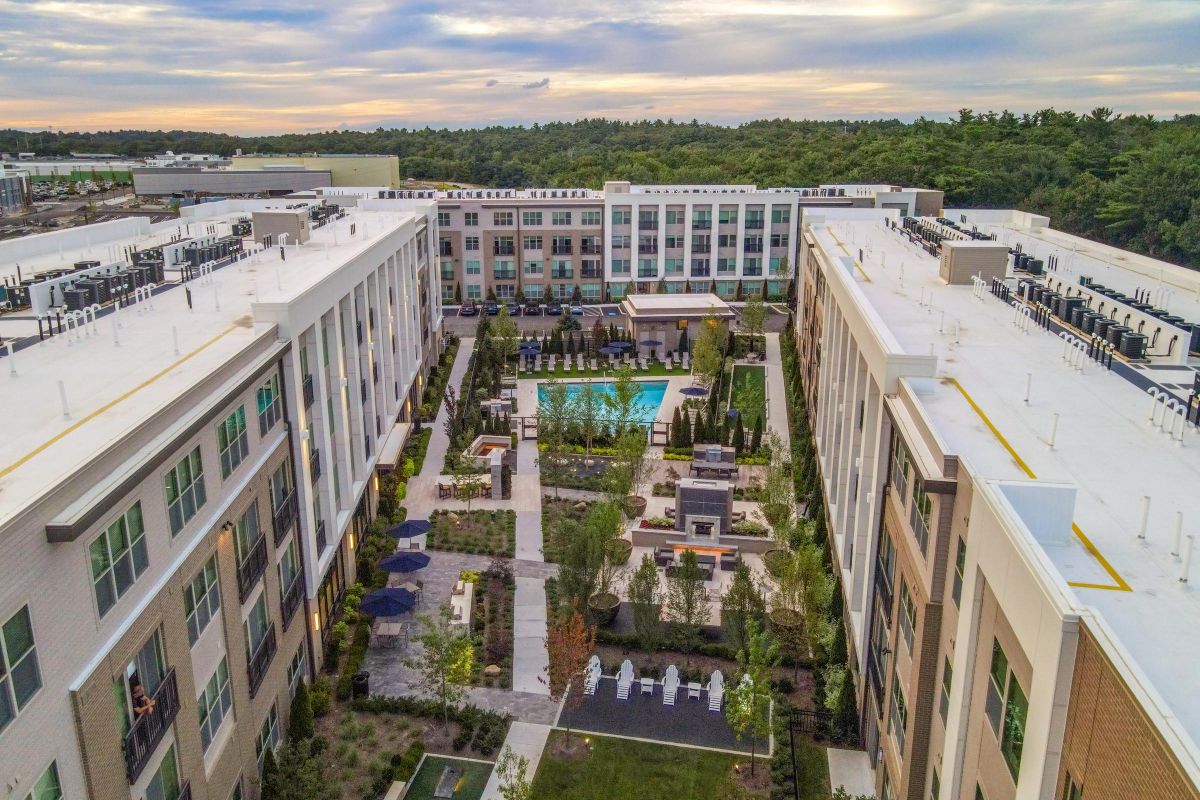 Aerial view of a modern apartment complex surrounding a courtyard with a pool and landscaped gardens.