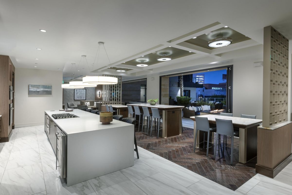 Modern kitchen with white marble floor, island, bar stools, and open patio view.
