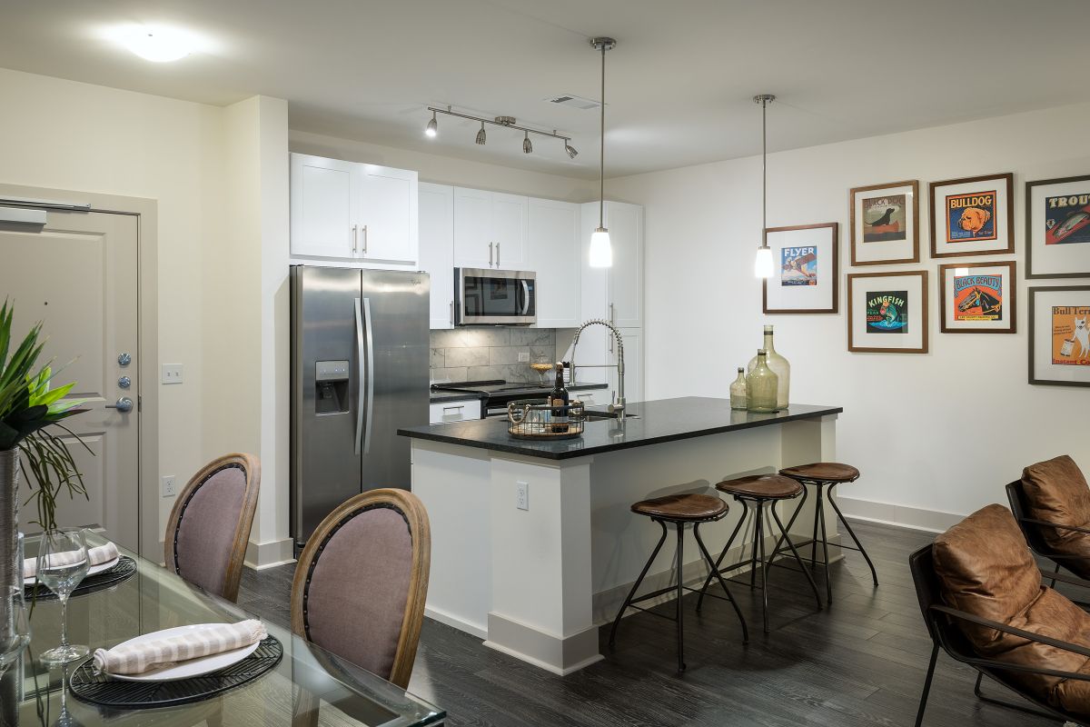 Modern kitchen with stainless steel appliances, barstools at an island, and dining area with framed art on the wall.
