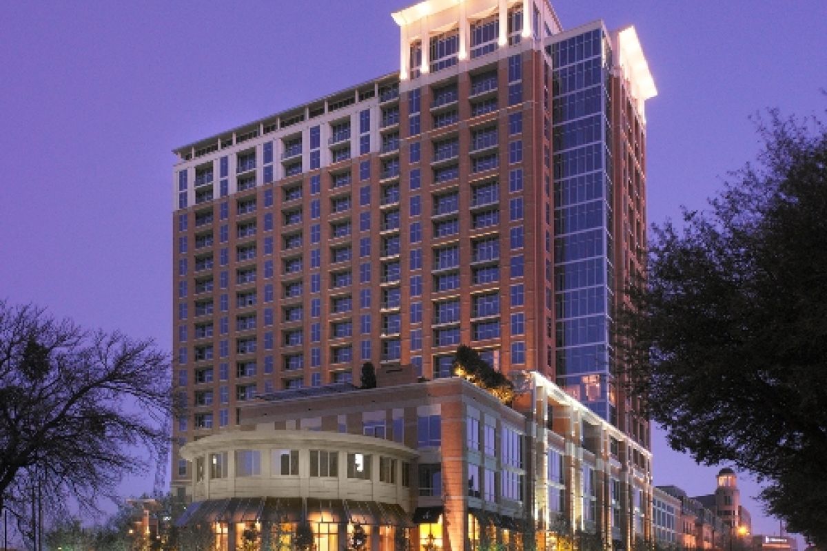 Tall, modern hotel building lit up at dusk with blurred car lights on the street in front.
