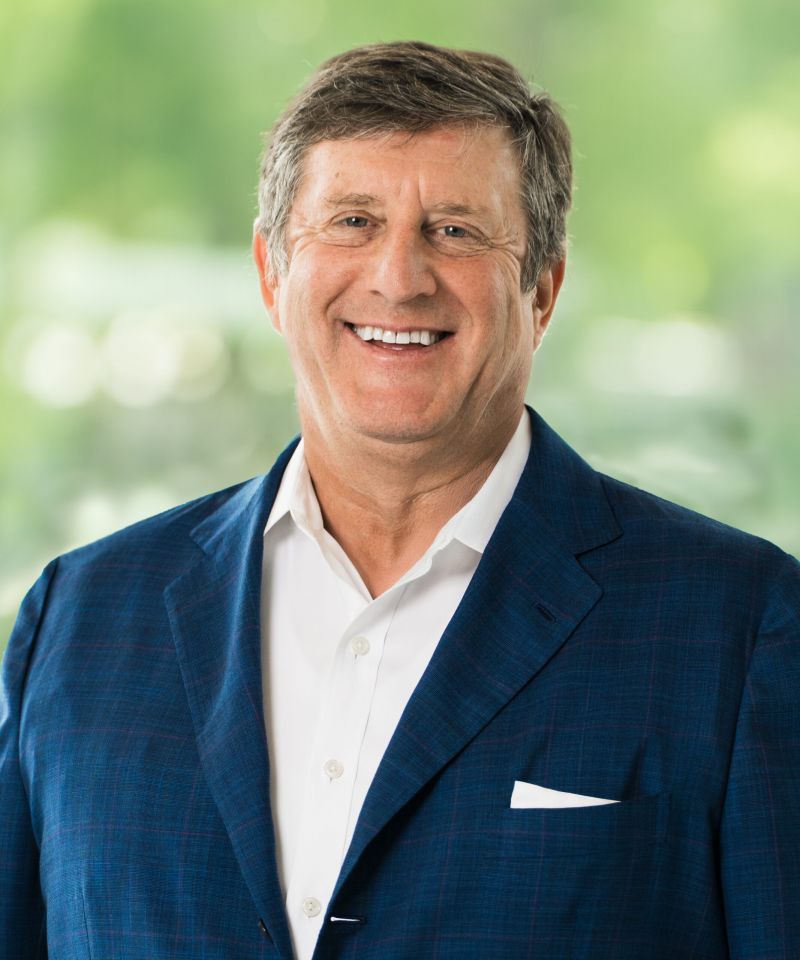 Smiling John Garibaldi in a blue suit jacket and white shirt stands before a blurred green background.