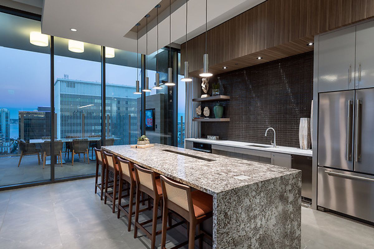 Modern kitchen with a marble island, wooden chairs, stainless steel appliances, and floor-to-ceiling windows.