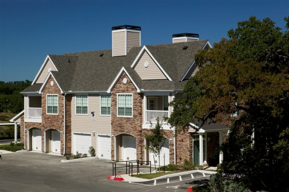 Two-story townhouse building with brick and siding exterior, garage doors, and a tree in front.