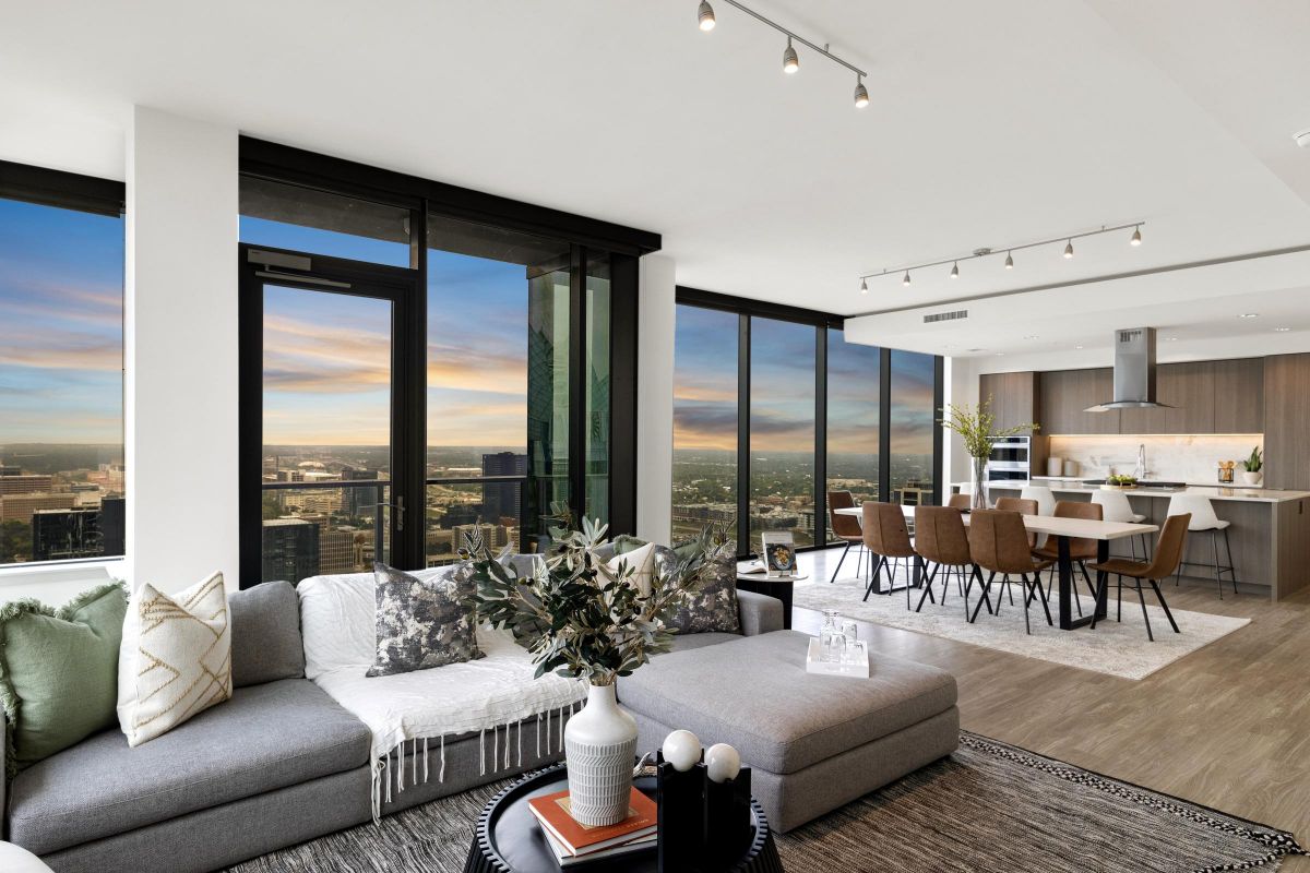 Modern open-plan living and dining area with city skyline views through large windows at sunset.