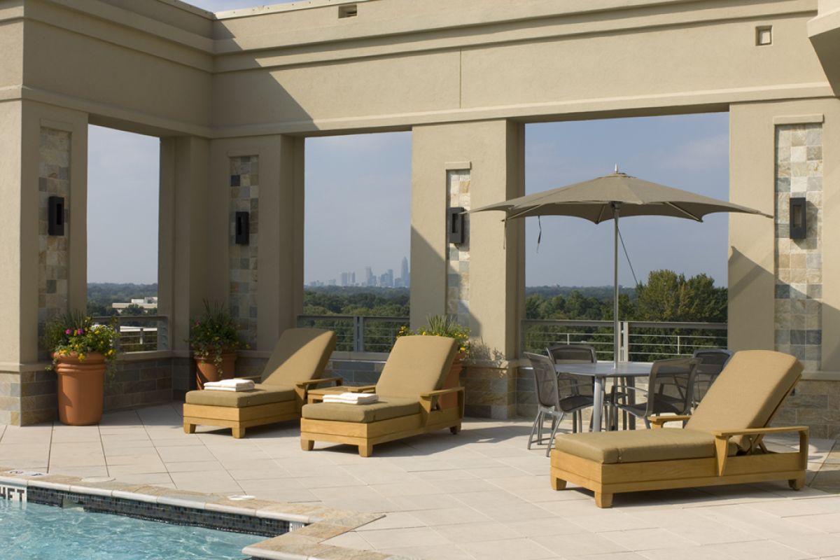 Three poolside lounge chairs and a table with umbrella overlook a city skyline in the distance.