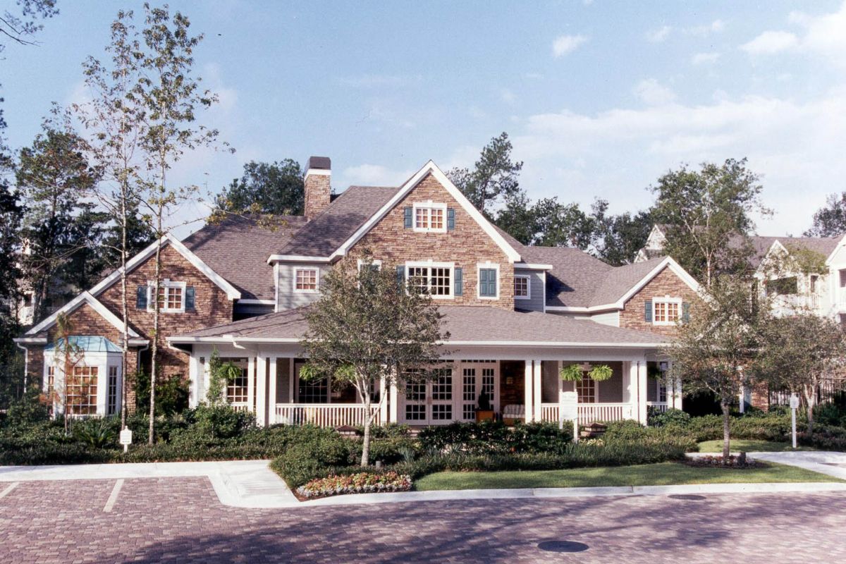 Large suburban house with brick exterior and wide porch at Churchill on the Park, surrounded by trees on a sunny day.