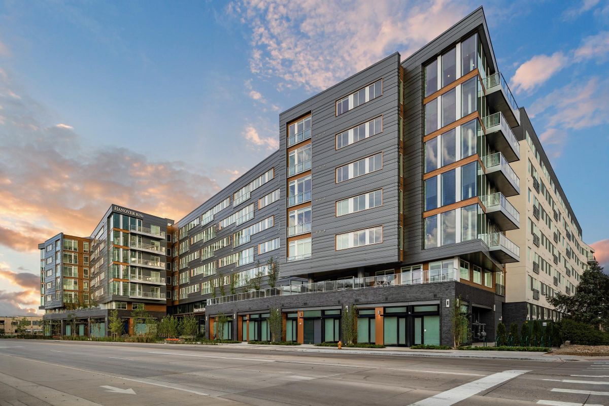Modern multi-story apartment building with large windows and balconies under a cloudy sky at sunset.