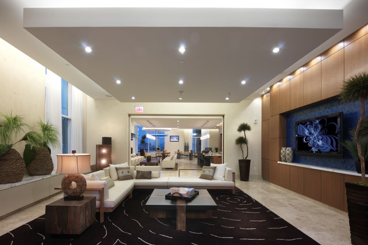 Modern living room with white sofas, potted plants, wooden accents, and a large TV on a blue accent wall.