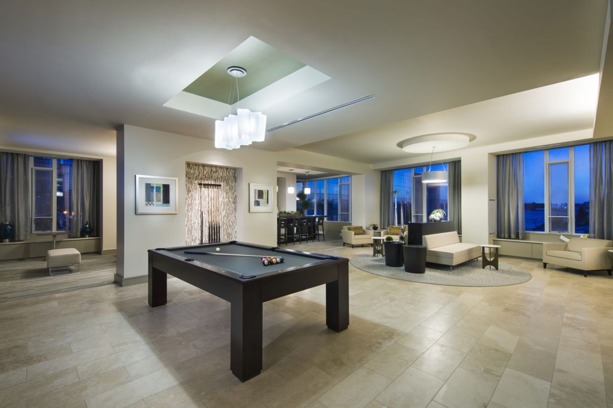 Modern lounge with a pool table, seating areas, large windows, and contemporary lighting.