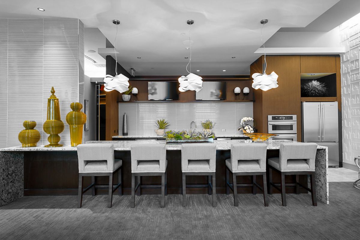 Modern kitchen with a large island, five chairs, and yellow decorative vases and bowls on the counter.