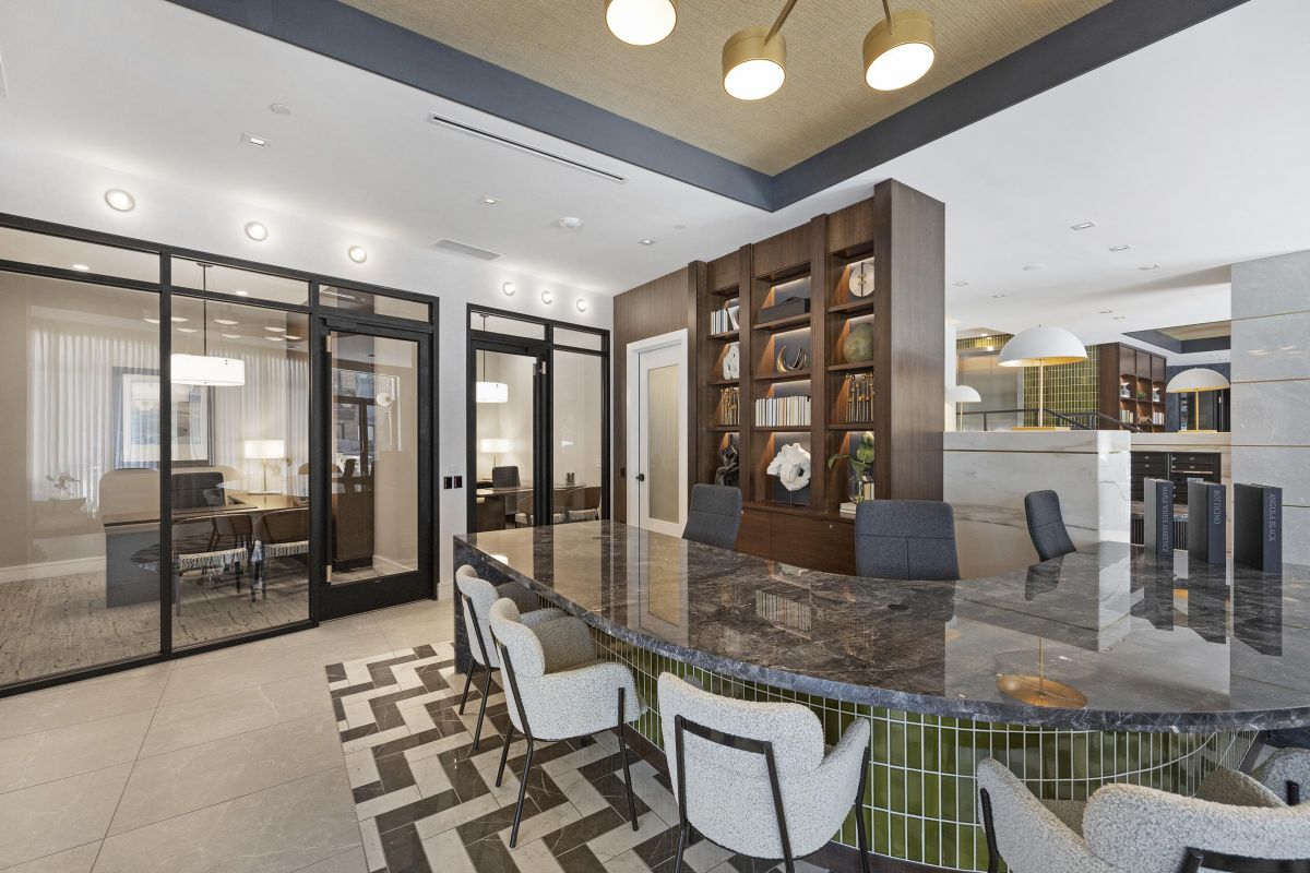 Modern office space with a large marble table, glass partitions, and bookshelves.