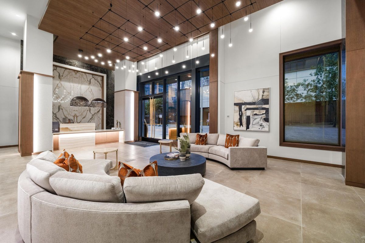 Modern lobby with curved sofas, hanging lights, large artwork, and wall-sized windows. Neutral tones and wood accents.