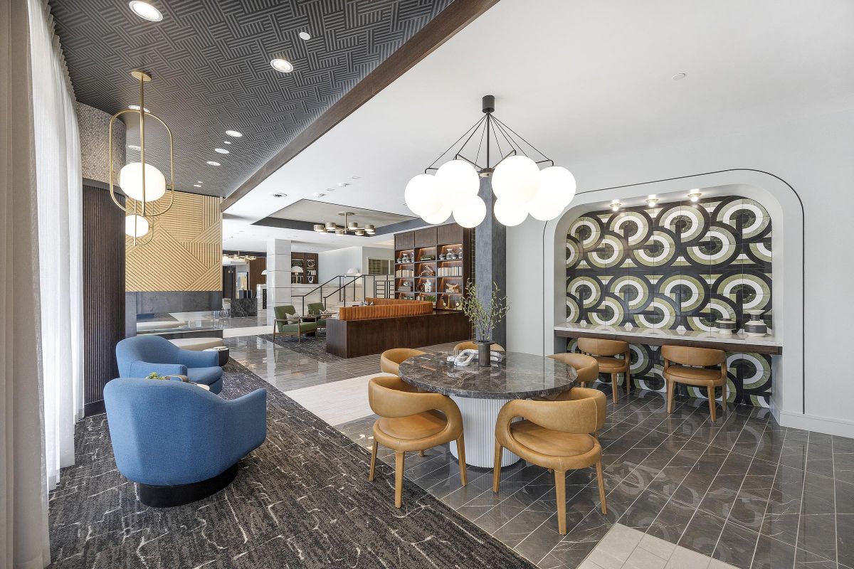 Stylish modern lounge with blue chairs, a round table, decorative wall, and a bookshelf in the background.