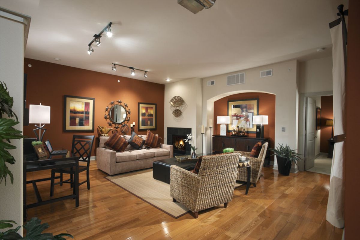 Modern living room with warm lighting, wooden floors, wicker chairs, and brown accent walls decorated with art.