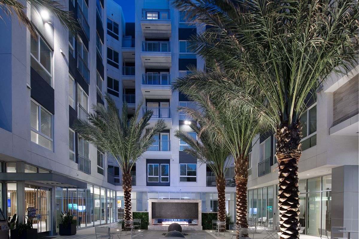 Modern apartment courtyard at dusk at Hanover Warner Center, with palm trees, outdoor seating, and a central fire pit.