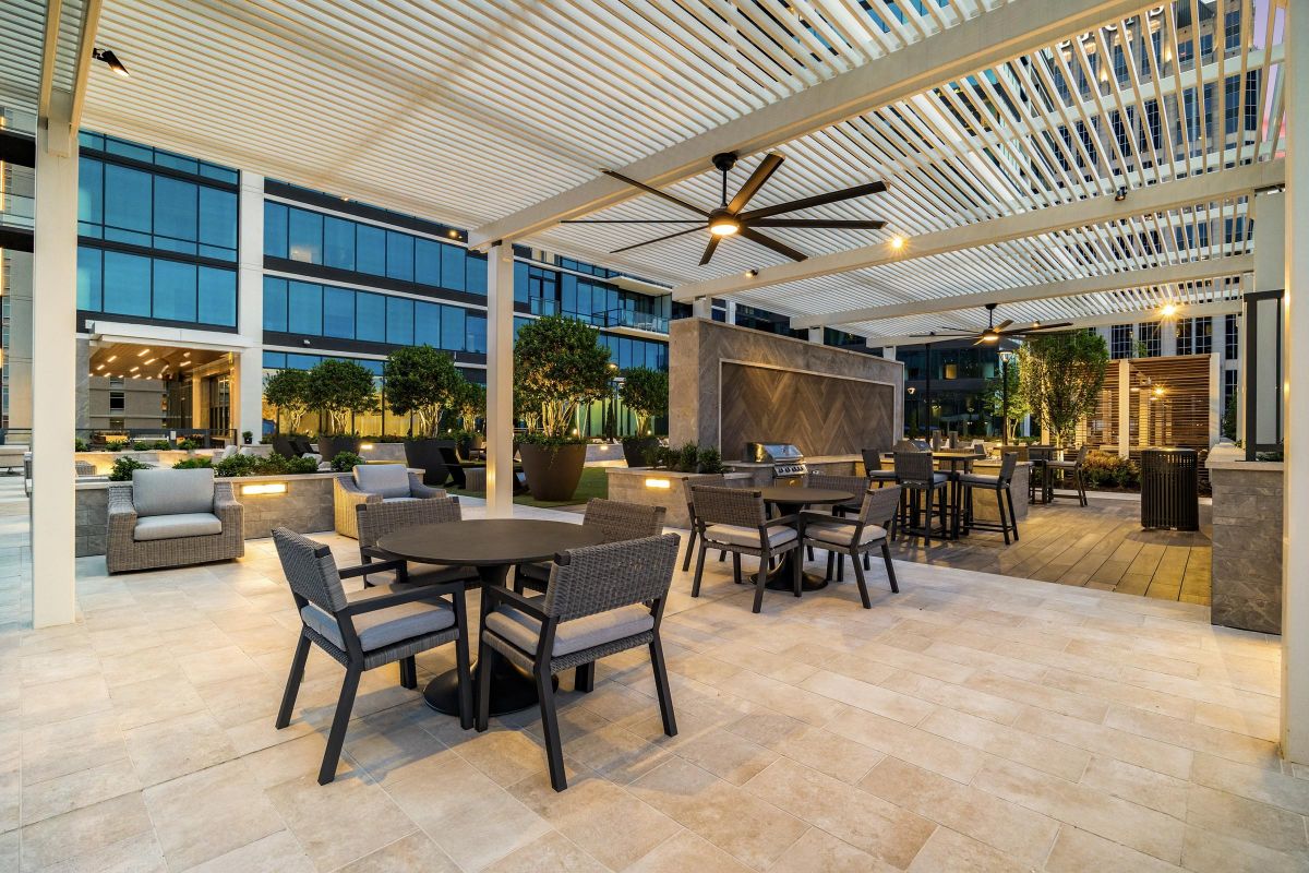 Outdoor patio with modern seating, tables, ceiling fans, and potted plants under a pergola at dusk.