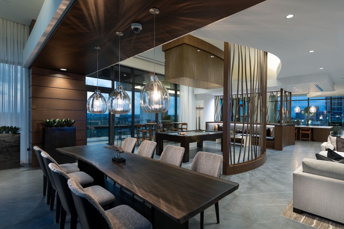 Modern, stylish lounge with pendant lights, long dining table, pool table, and floor-to-ceiling windows.