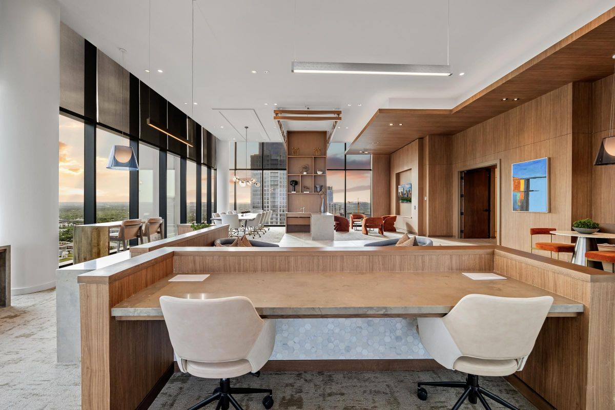 Modern office space with wooden furniture, large windows, and a city view at sunset. Art decorates the walls.