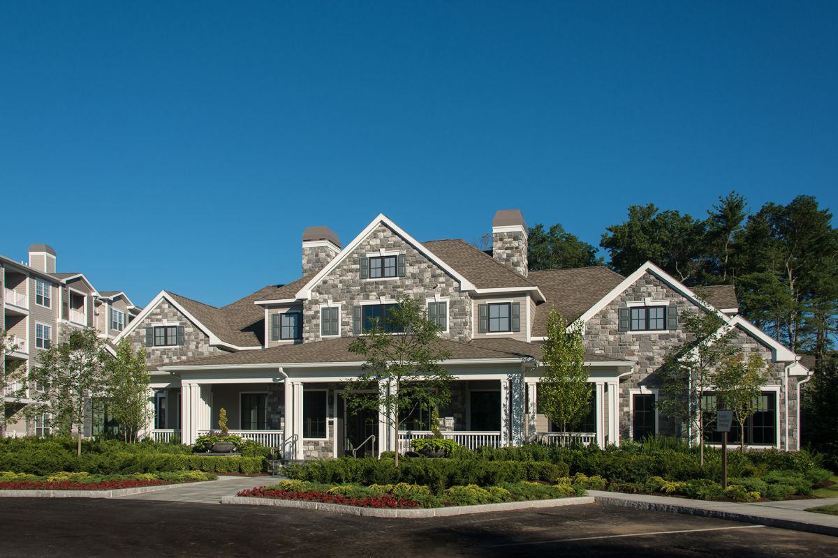 Large stone house with white trim, front porch, and landscaped garden under a clear blue sky.