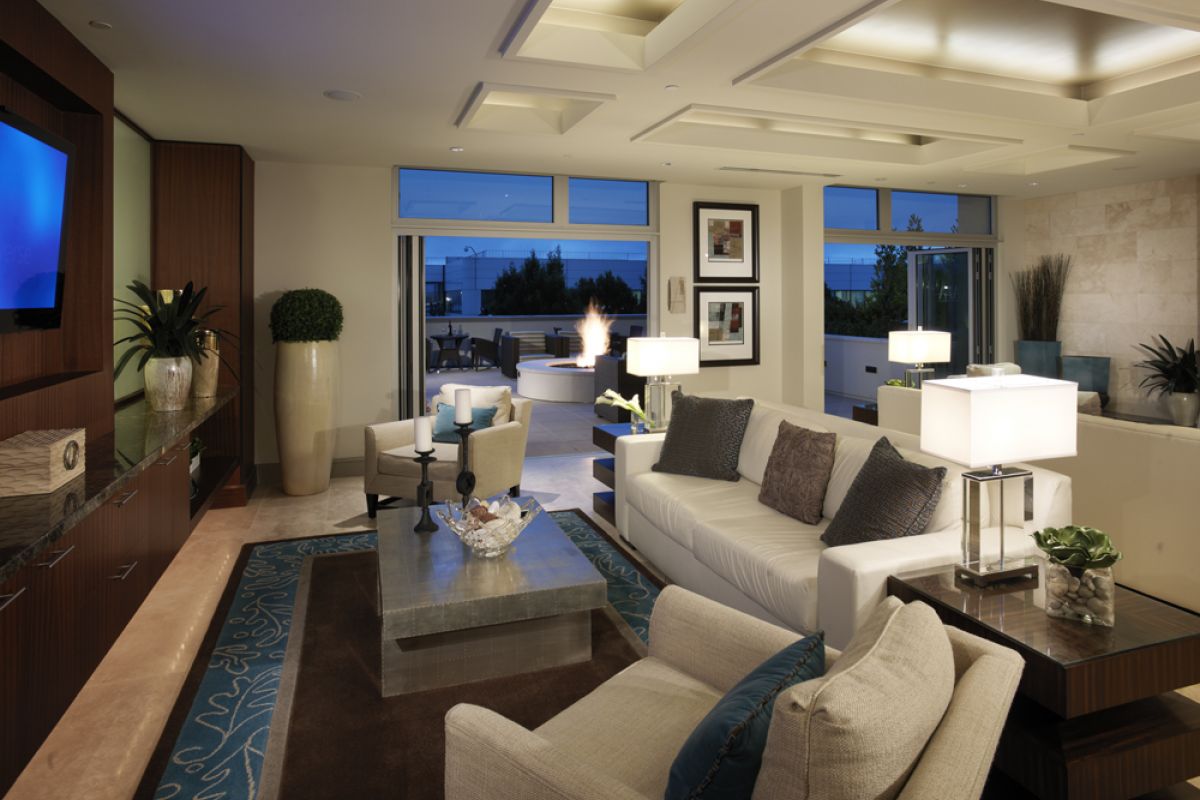 Modern living room with neutral decor, large windows, and a view of the Ashton Candlestick Cove patio at dusk.