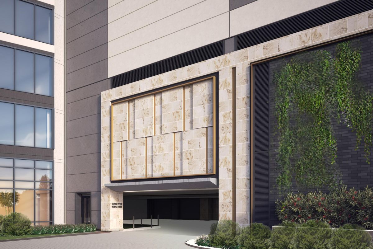 Modern building entrance with a stone facade and vertical garden on the side, leading to an indoor parking area.