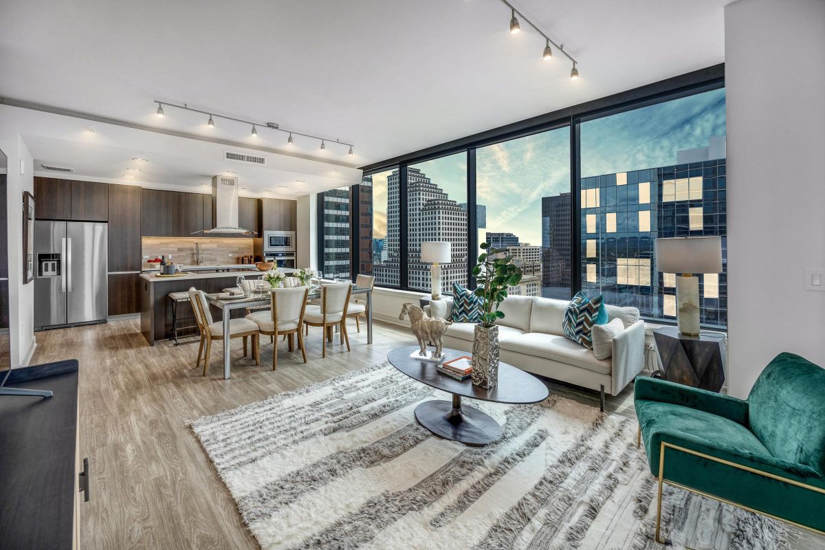 Modern open-concept living room and kitchen with city views through large floor-to-ceiling windows at sunset.