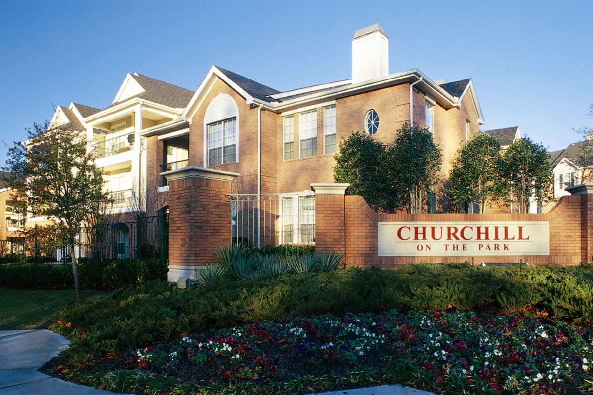 Red-brick Dallas apartments with a "Churchill on the Park" sign and landscaped flowers in front.