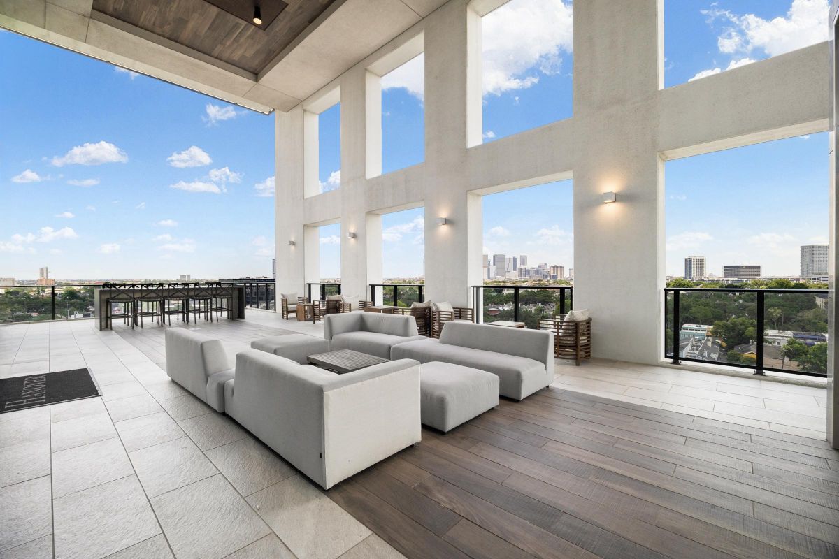 Spacious outdoor terrace with modern seating, high ceiling, and city skyline views under a clear blue sky.