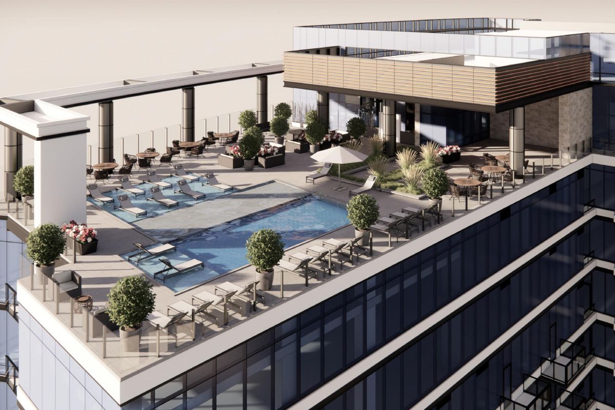 Rooftop pool with lounge chairs, tables, and greenery on a modern high-rise building.