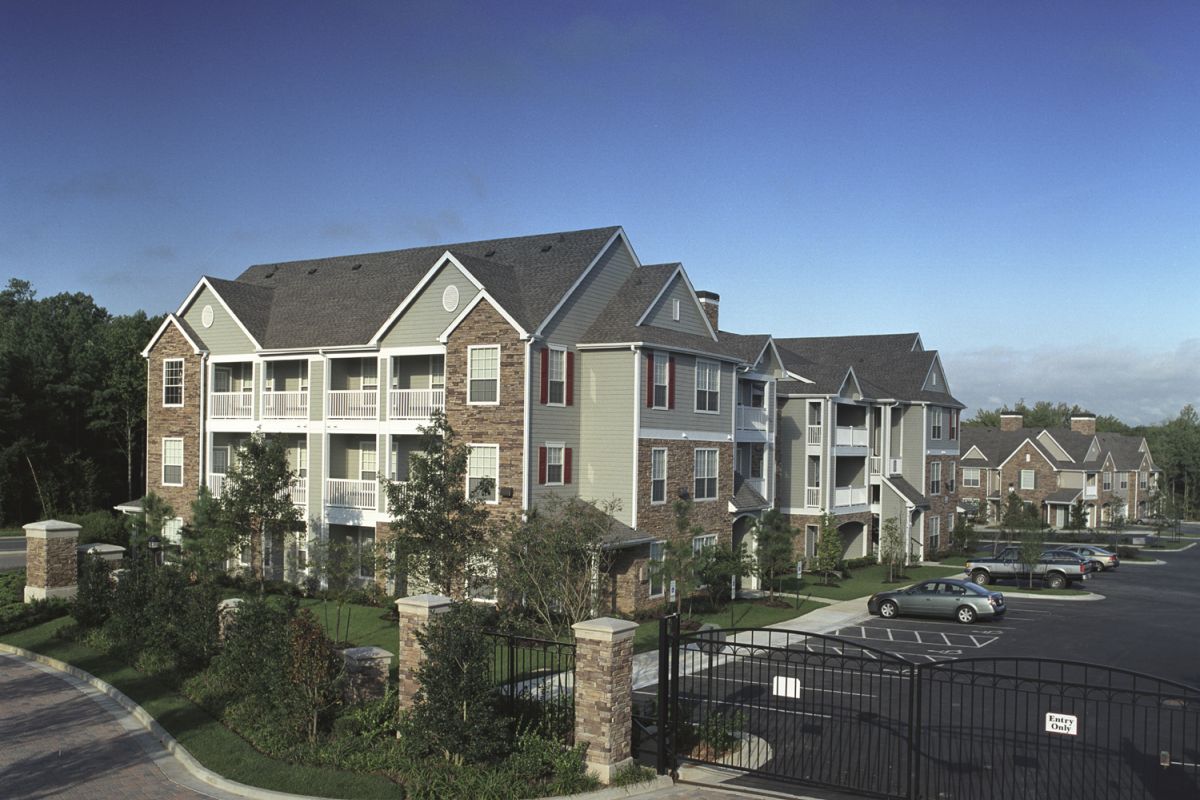 Gated apartment complex with parked cars, landscaped grounds, and multi-story residential buildings.