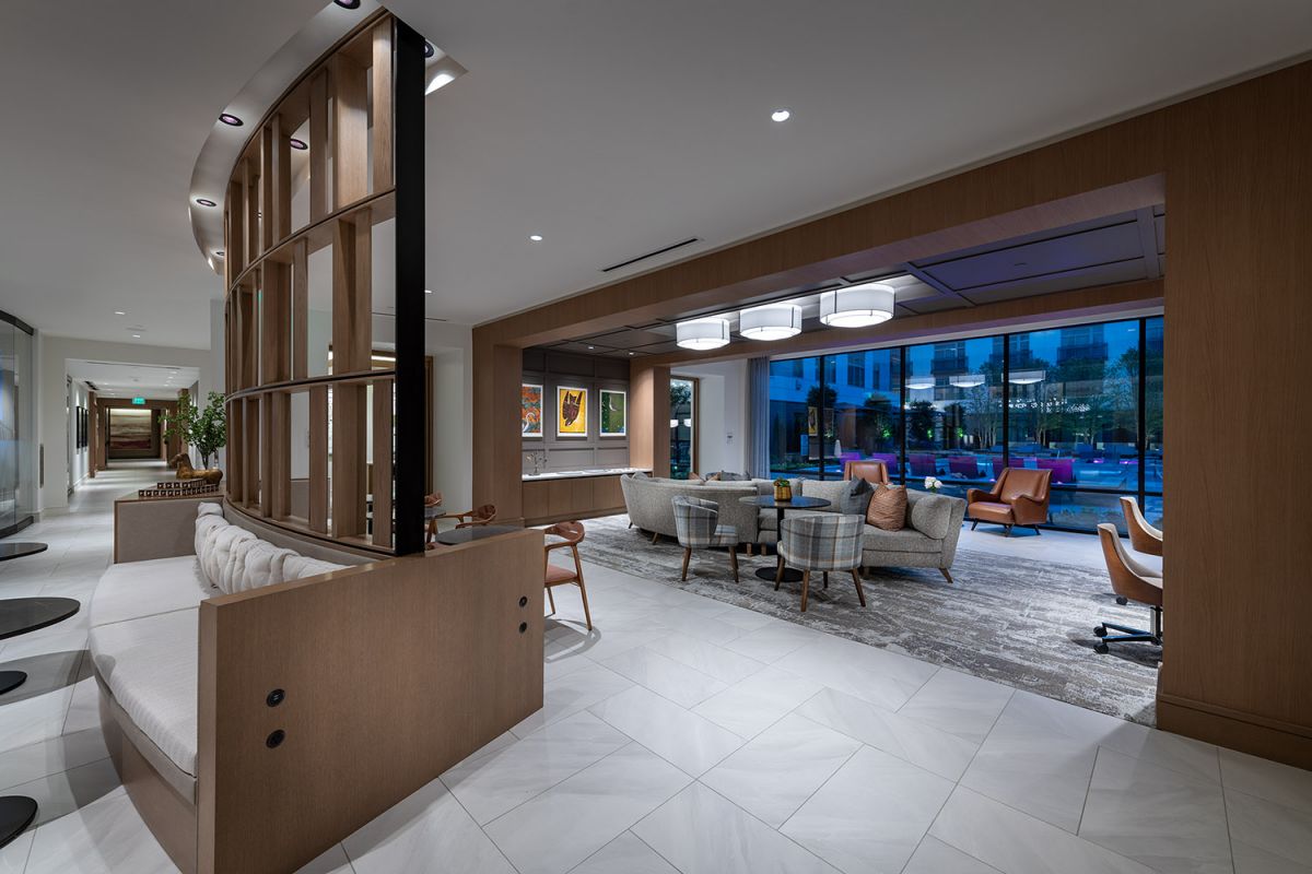 Modern hotel lobby with wood accents, ample seating, and large windows overlooking an outdoor area at dusk.
