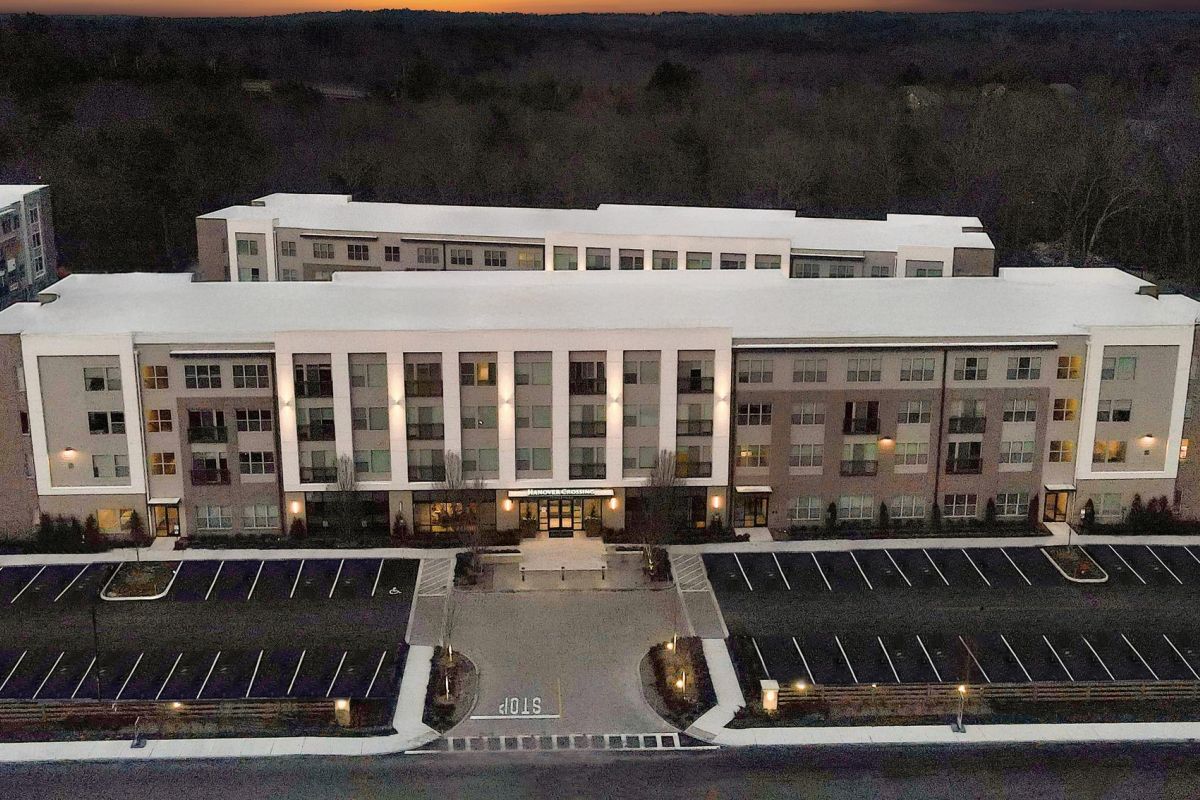 A large, modern apartment building with empty parking lots in front, surrounded by trees at dusk.