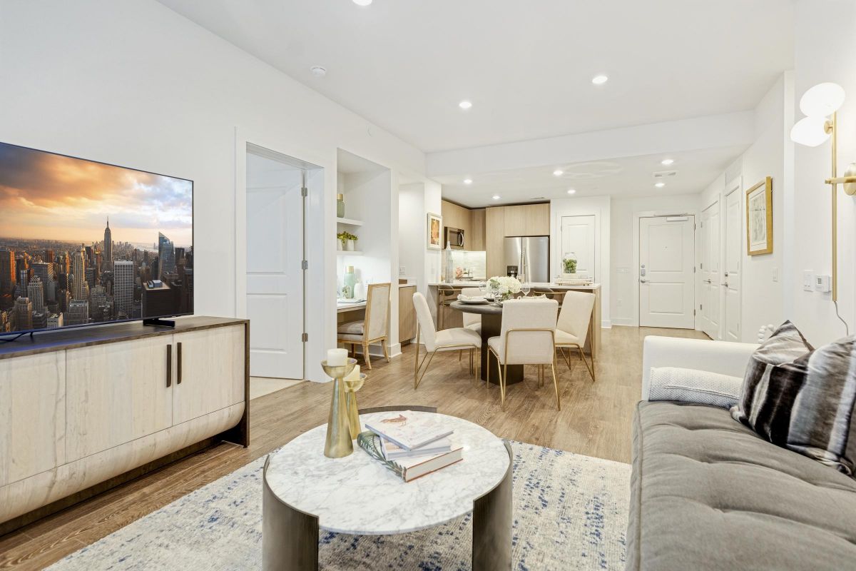Modern living room with a TV, a marble coffee table, a gray sofa, and a view into an open kitchen and dining area.