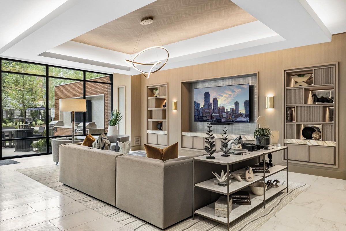 Modern living room with a large TV, gray sofa, decor items, and glass doors opening to a patio with outdoor furniture.