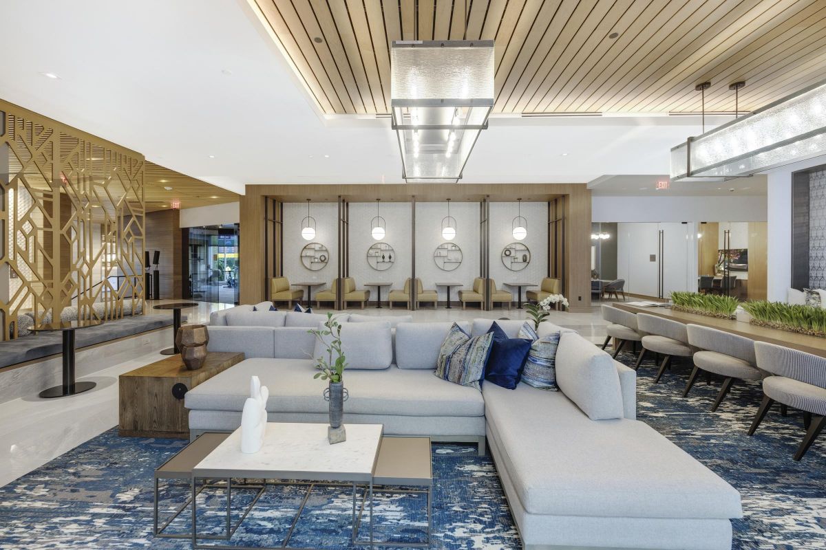 Modern hotel lobby with a gray sectional sofa, blue-patterned rug, and circular lighting fixtures above seating area.