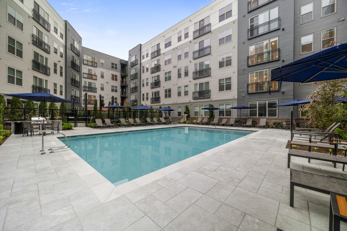 Modern Hanover apartment complex with a swimming pool, lounge chairs, and blue umbrellas in the Stoneham courtyard.