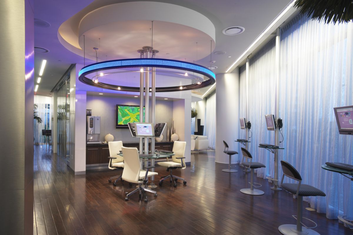 Modern office with sleek furniture, wood floors, blue lighting, and computer stations by large curtained windows.