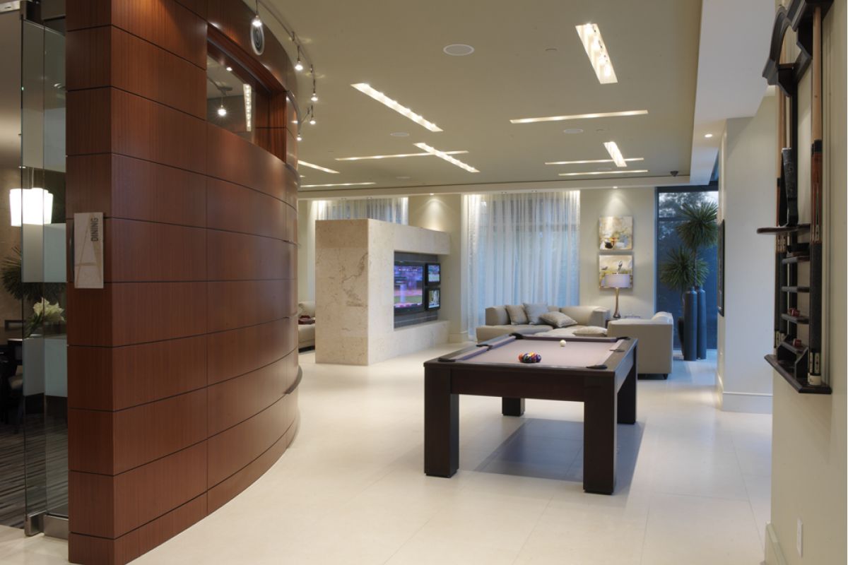 Modern living room with a pool table, TV, curved wood wall, and large windows with sheer curtains.