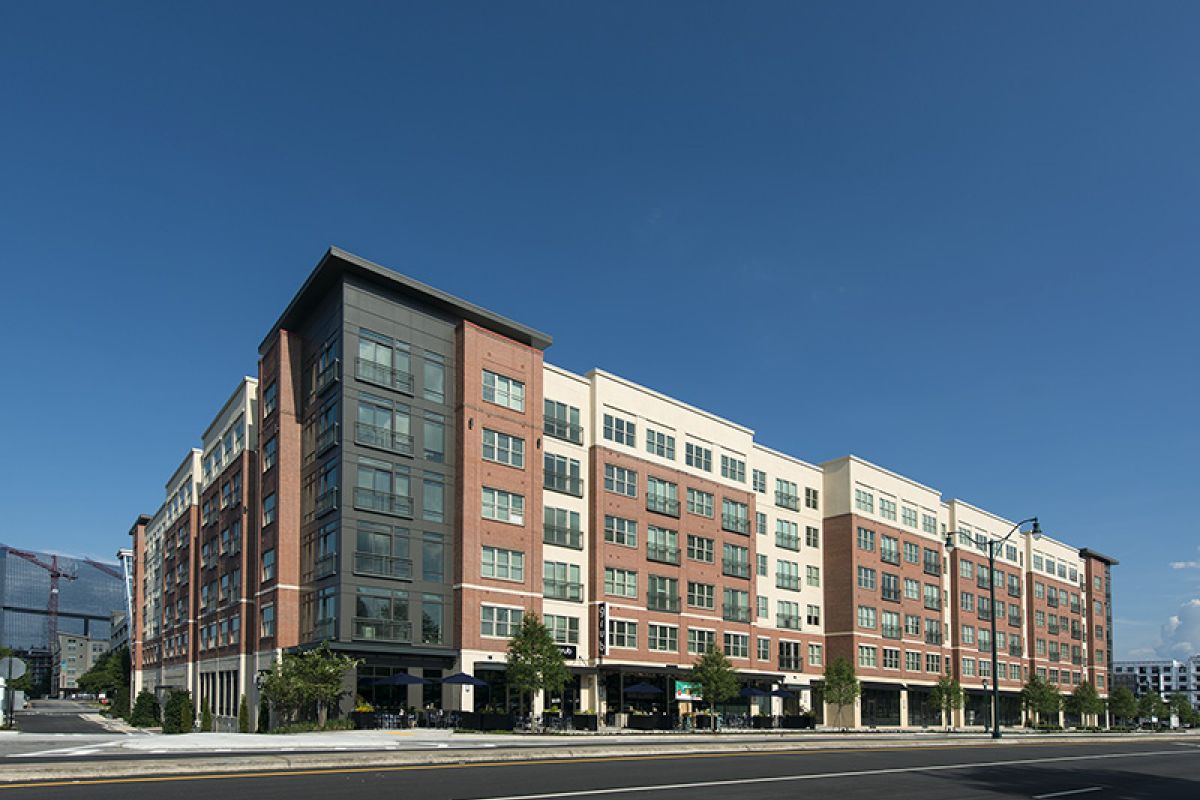 Modern mid-rise apartment building with shops on ground floor under a clear blue sky.