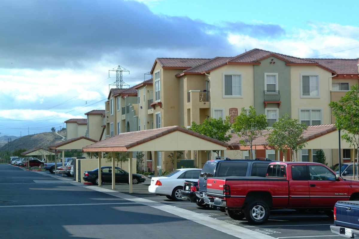 Row of apartment buildings with parked cars under carports on a cloudy day.